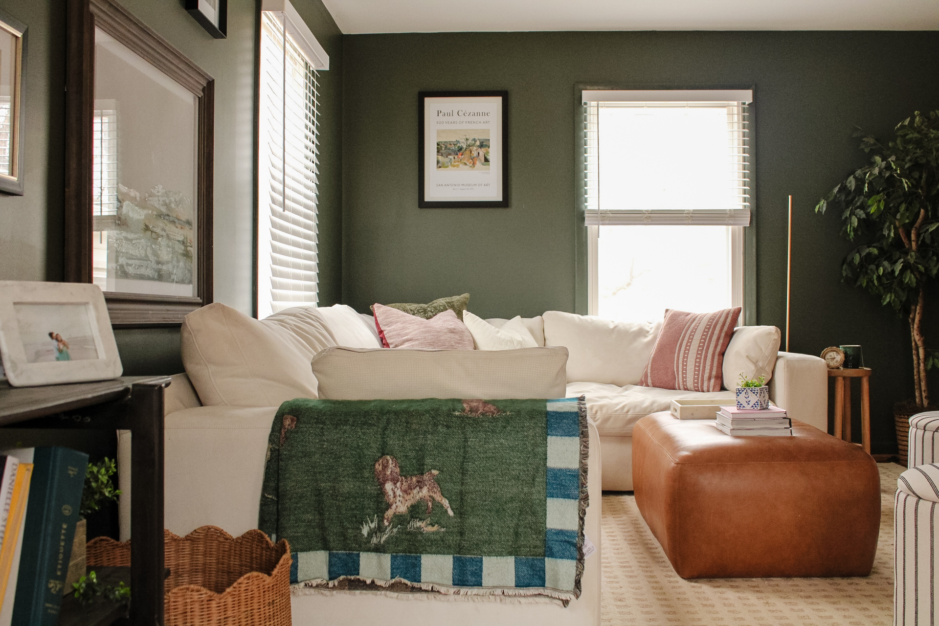 Living room with deep green walls, cream sectional, and leather ottoman